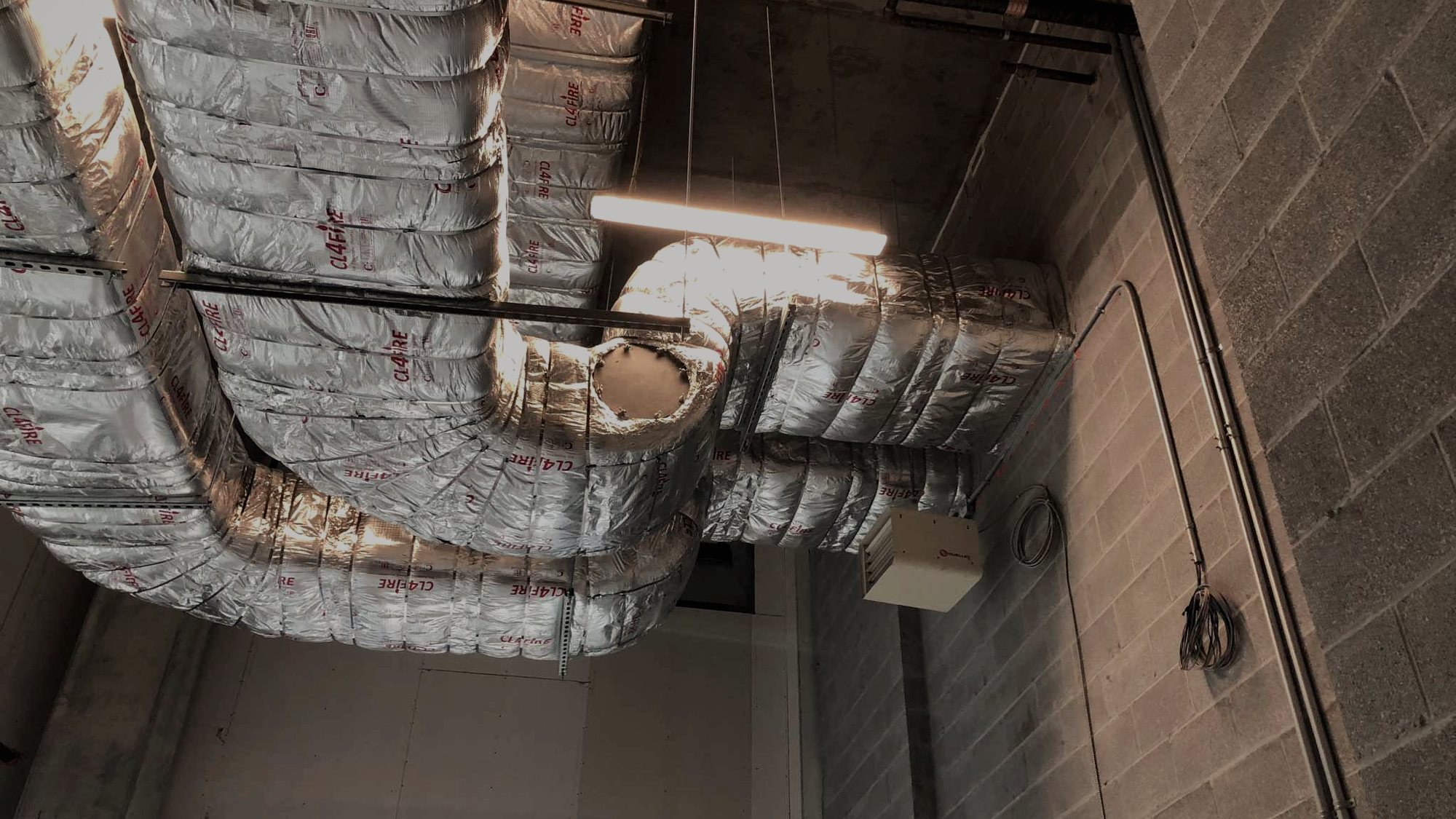 Fire-wrap being installed over ductwork under work lights.